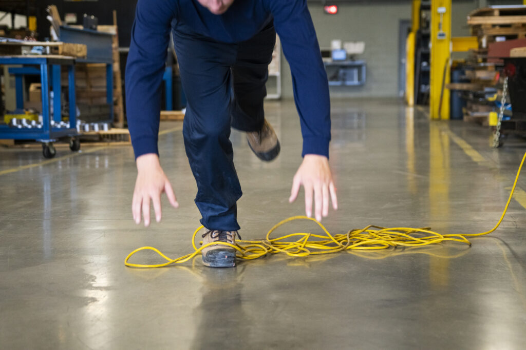A worker tripping over a yellow extension cord in an industrial setting
