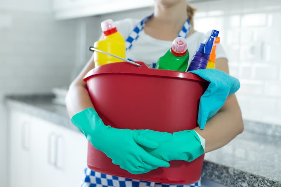 Woman holding a red bucket full of cleaning supplies
