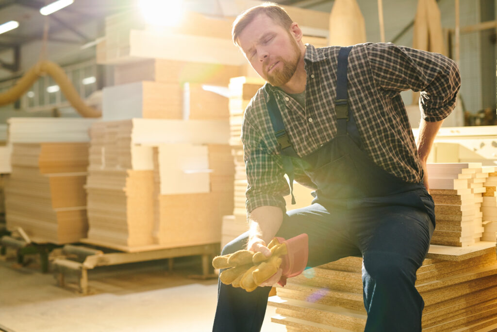 Worker with back pain sitting on a stack of lumber
