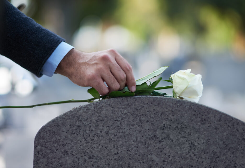 A man placing a white rose on top of a gravestone