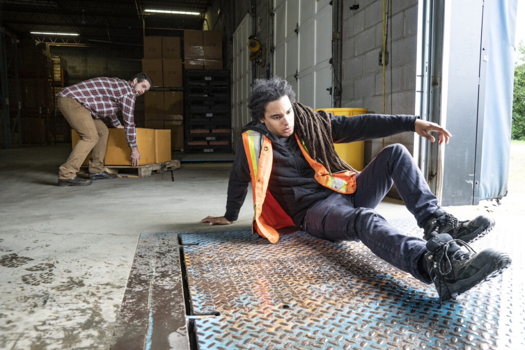 A warehouse worker slipping and falling on a wet loading dock with a coworker in the background