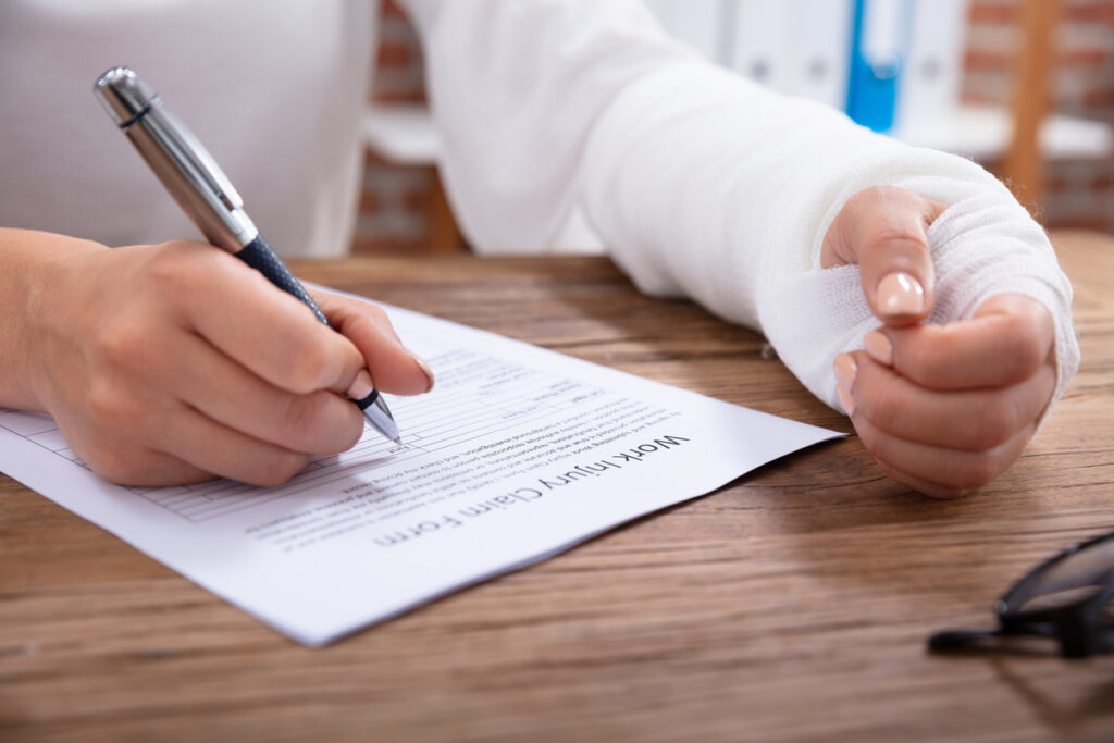 Close-up of a woman with a bandaged hand filling out a work injury claim form