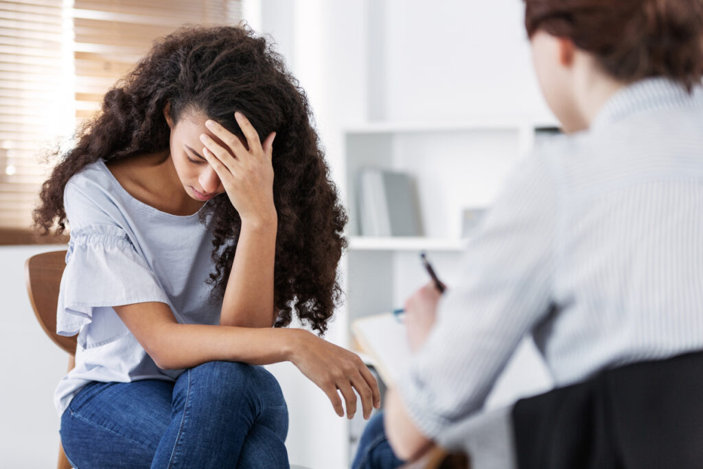 A distraught young woman holding her head while talking to a therapist