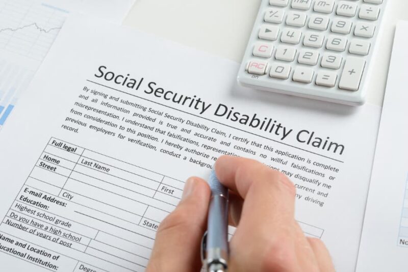 Close-up of a person’s hand filling out a Social Security Disability form with a calculator above it