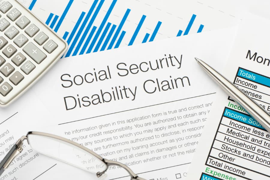 Close-up of a Social Security Disability claim form with a pen, calculator, and eyeglasses.