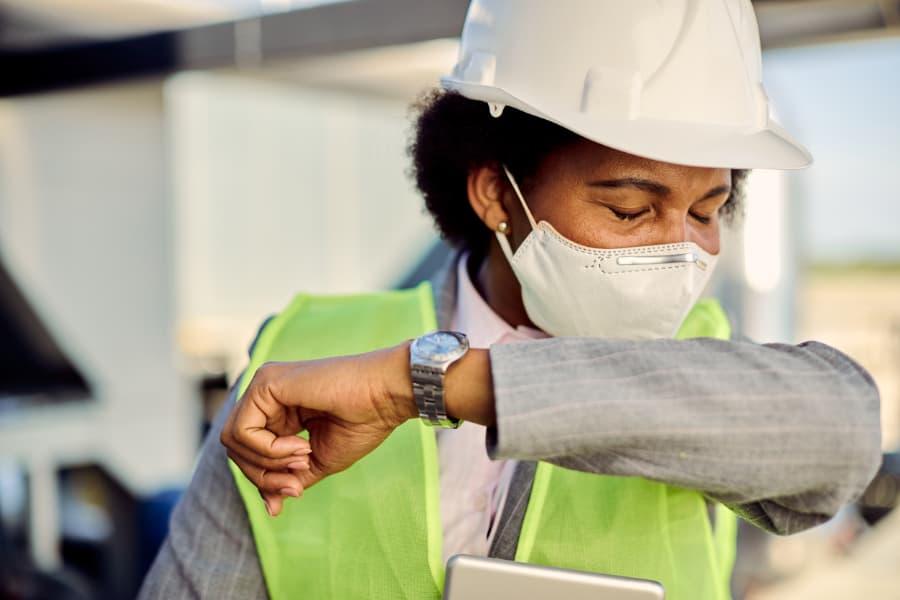 Woman wearing protective face mask while coughing into her elbow at construction site