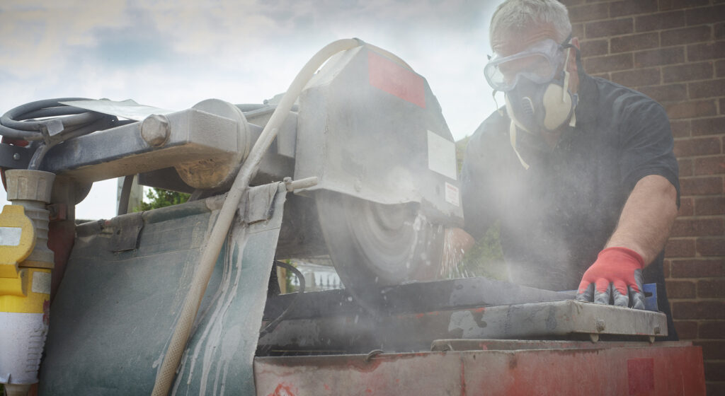 A worker cutting concrete with a cloud of dust around him