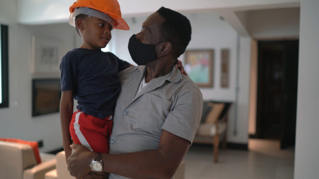 Man with black mask holding little boy with orange hardhat